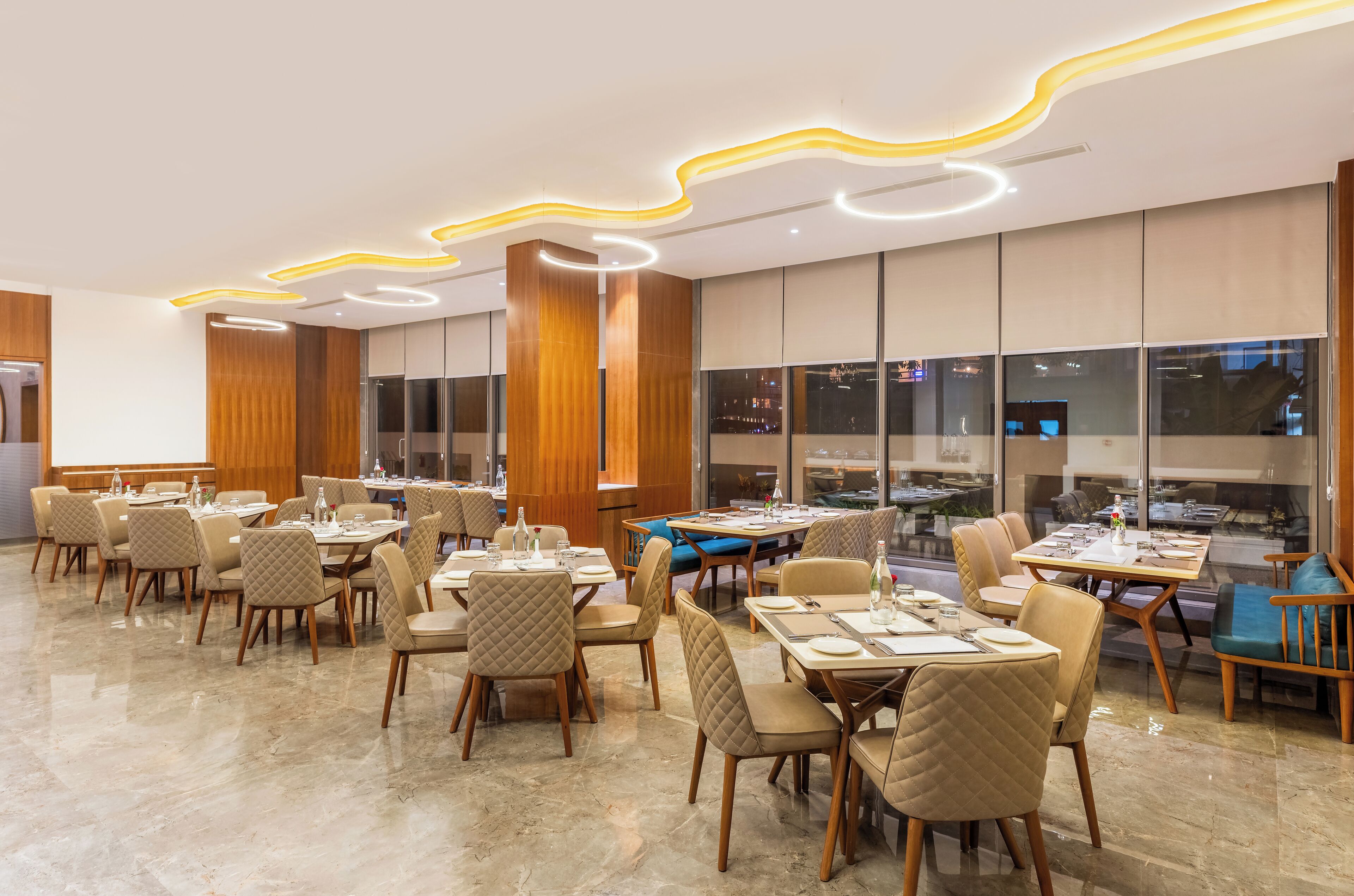 Un comedor moderno con mesas y sillas, ventanas amplias y un diseño contemporáneo en el techo.