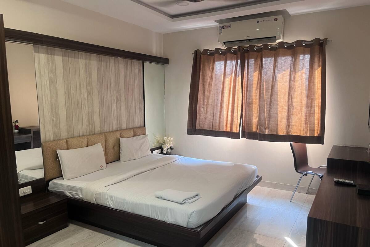 A neatly arranged bedroom with a large bed, a bedside table, a desk, and a window with curtains.