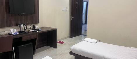 A hotel room with two beds, a desk with a computer, a flat-screen TV mounted on the wall, and a small kitchenette area.