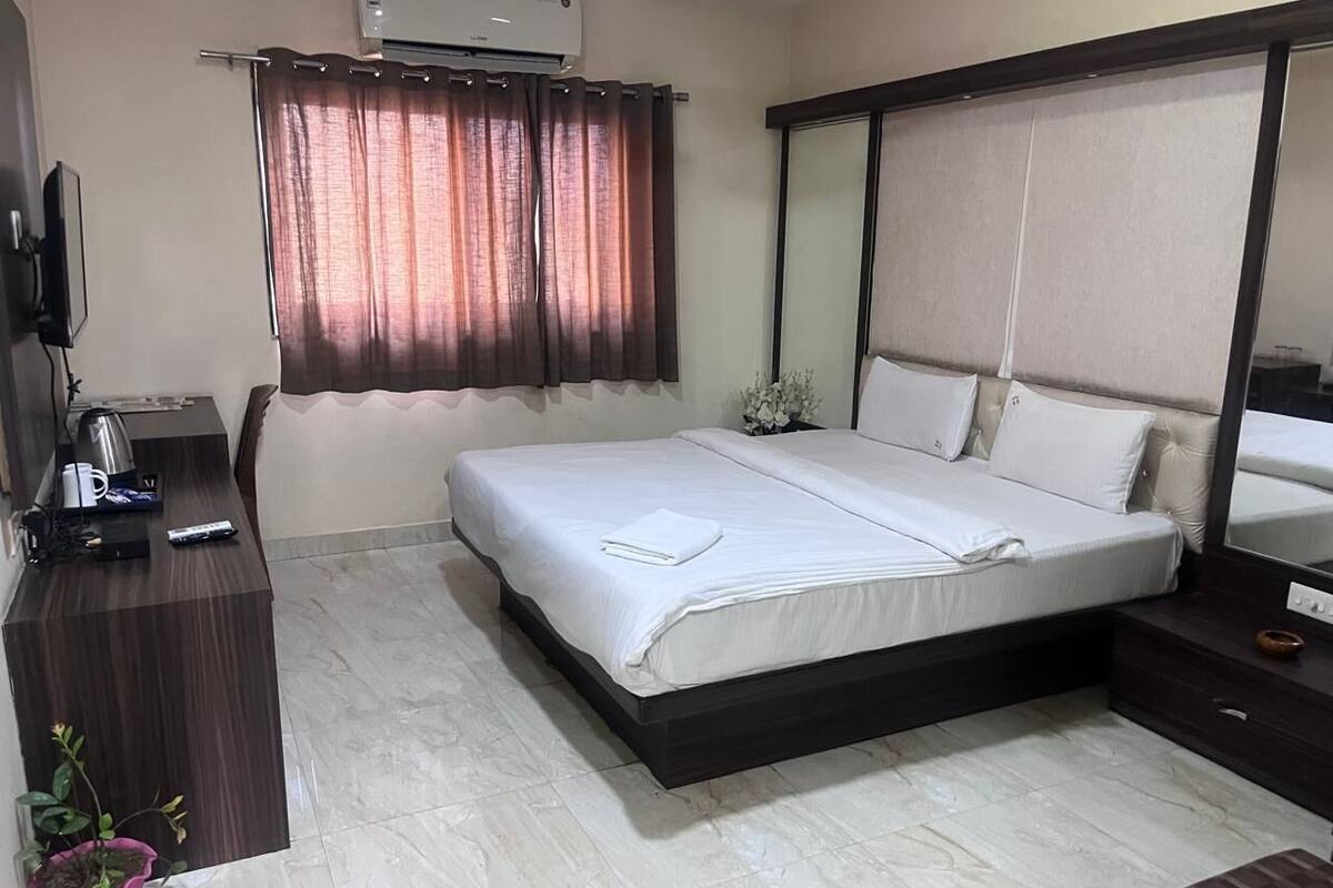 A bedroom with a bed, a bedside table, a TV, a potted plant, and a window with curtains.