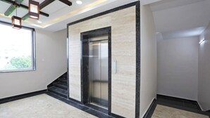 An elevator in a modern building with a marble wall and black accents.