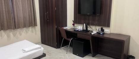 A hotel room with a bed, a desk with a computer, a TV, and a wardrobe.