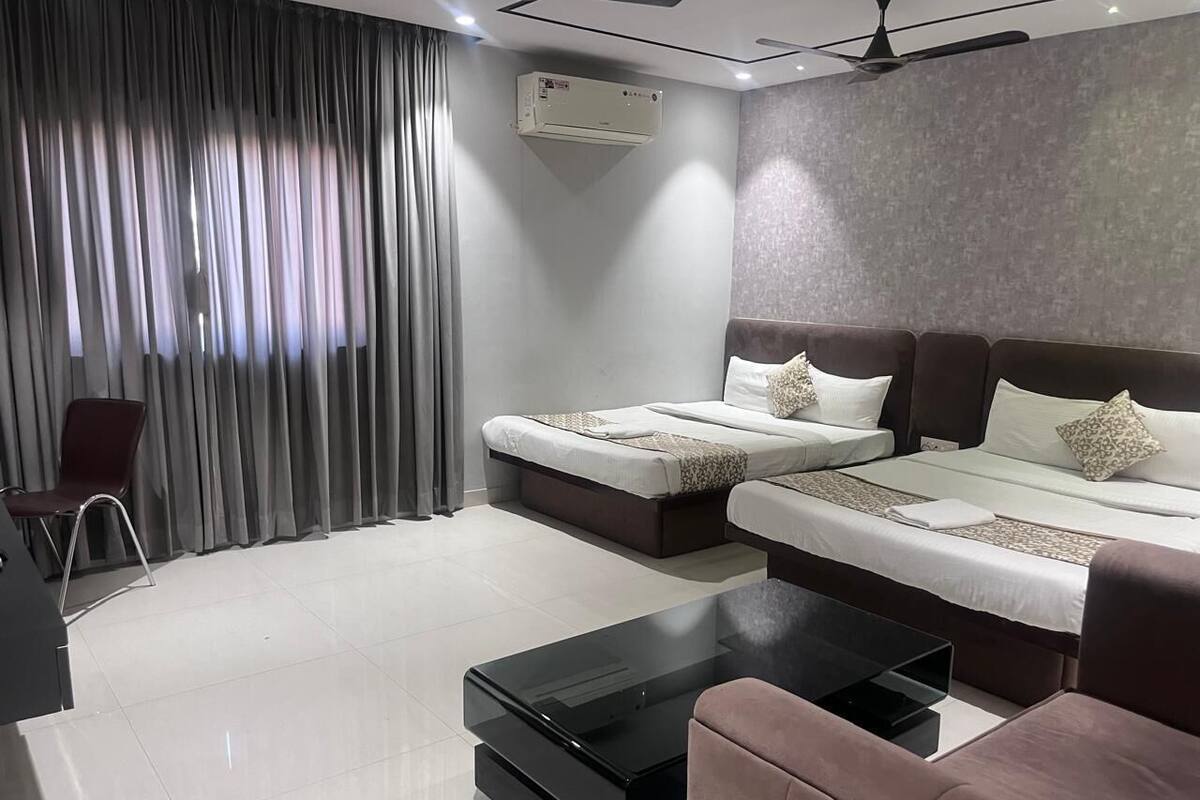 A modern hotel room with two beds, a flat-screen TV, a coffee table, and a ceiling fan.