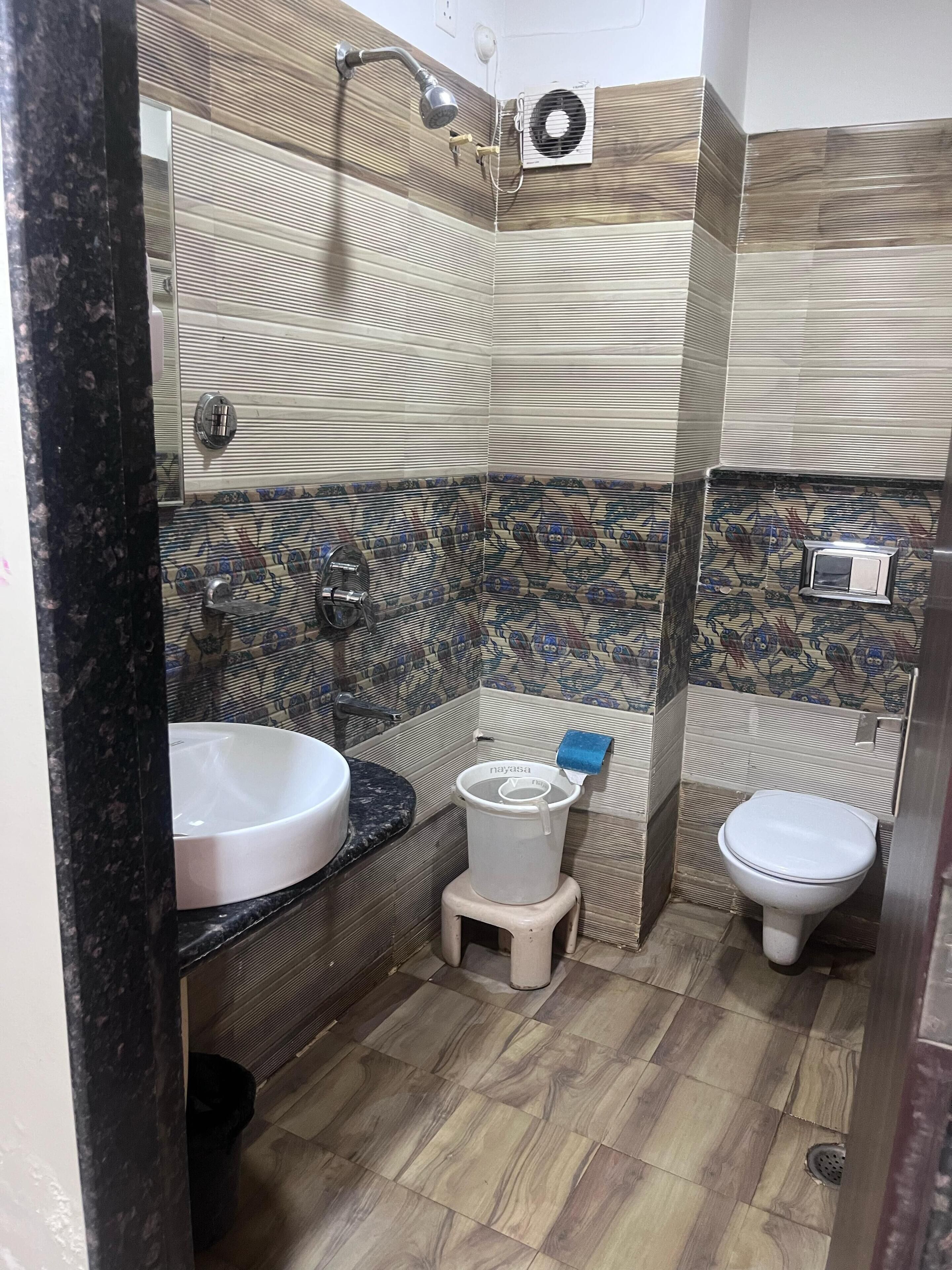 A bathroom with a marble sink, a shower with a handheld showerhead, a toilet, and a wall-mounted air conditioning unit.