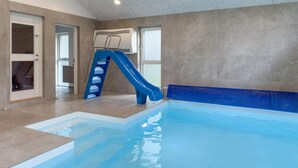 An indoor swimming pool with a blue slide, tiled walls, and a clear ceiling. - Lovely home in Ebeltoft (Ebeltoft)