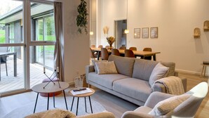 A modern living room with a sofa, armchairs, a coffee table, and a dining area in the background. - Lovely home in Ebeltoft (Ebeltoft)