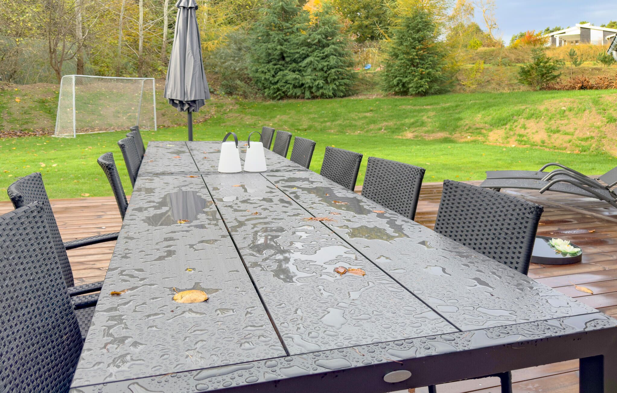 Une table rectangulaire pour l’extérieur, dotée d’un cadre en métal et d’un plateau de table de couleur sombre, entourée de huit chaises noires à dossier tressé.