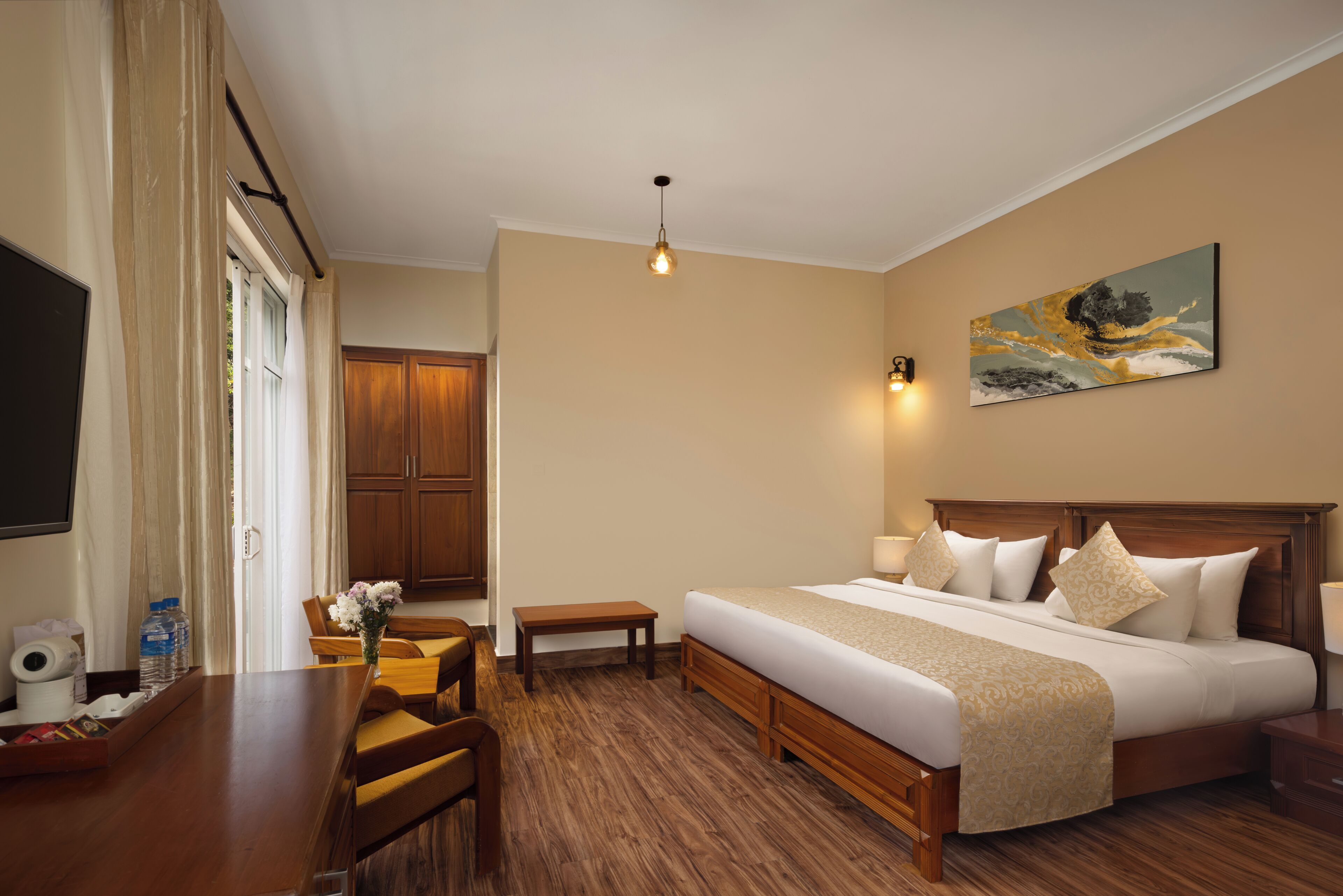 A hotel room with a bed, bedside tables, a desk, a chair, a small table with a vase of flowers, a painting on the wall, and a television.