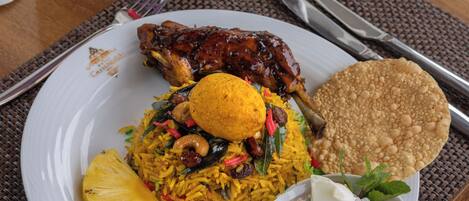 Un plato de comida con arroz, un trozo de carne, algo frito y un bol pequeño de ensalada.