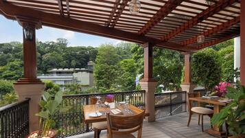 An outdoor patio with a wooden pergola, tables set for dining, and potted plants.