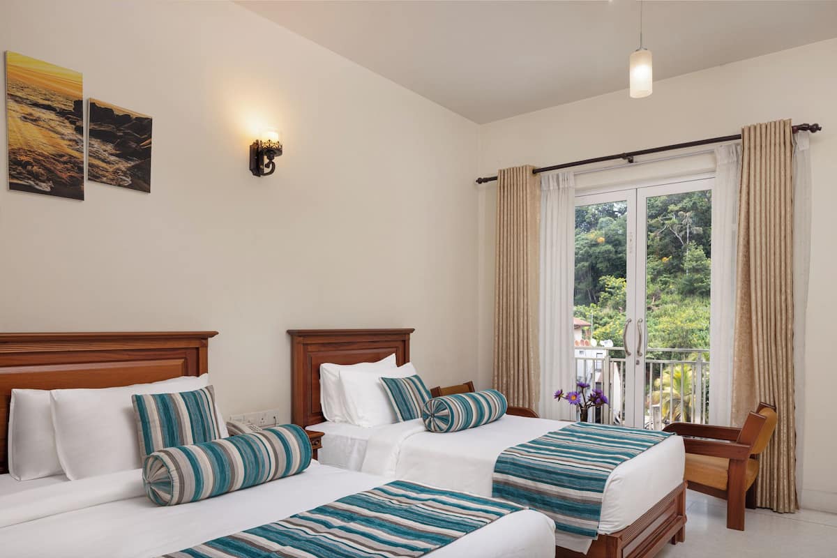 Habitación de hotel con dos camas, cabecero de madera, mesita de noche, lámpara de pared y ventana con cortinas.