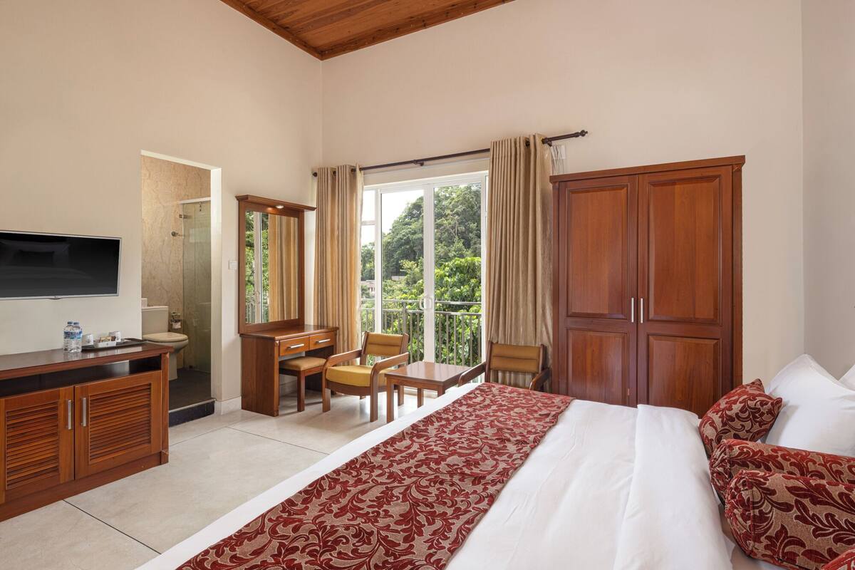 Habitación de hotel con cama, escritorio con silla, televisor, armario y balcón con cortinas.