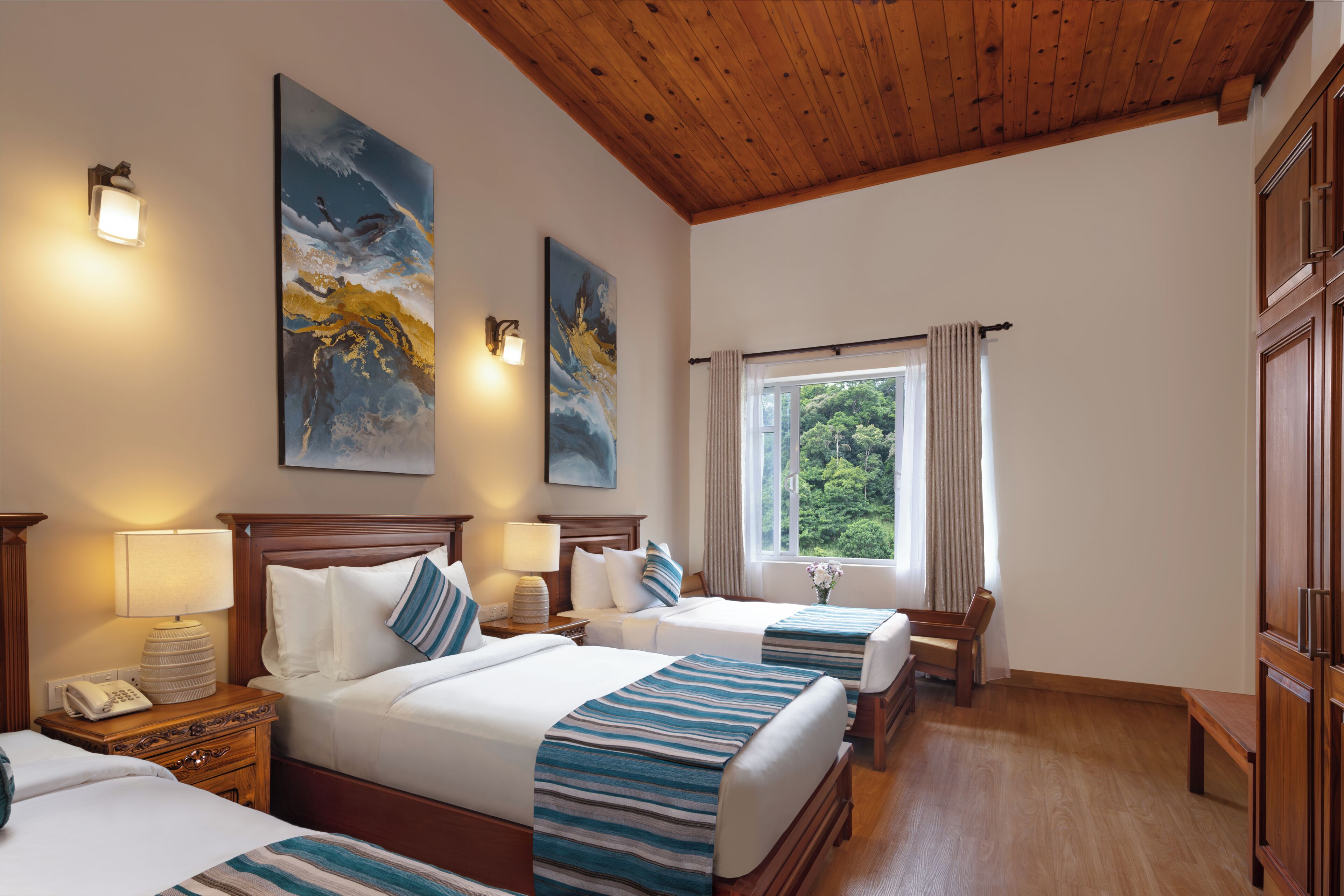 Une chambre d’hôtel avec deux lits, un plafond en bois, une fenêtre avec des rideaux et des œuvres d’art accrochées aux murs.