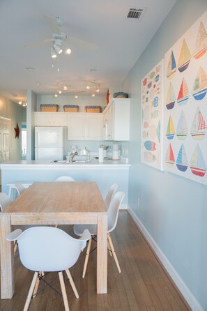 A modern kitchen with white cabinets, a central island, and a dining area with a wooden table and white chairs. - Walk to South Beach, Pier, Bars, Restaurants (Tybee Island)