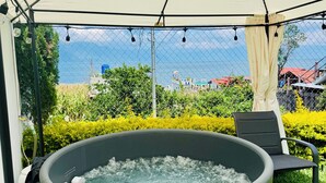 A hot tub under a canopy with a view of the sea and greenery.