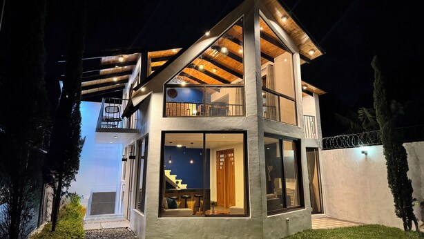 A modern two-story house with a balcony, large windows, and a staircase leading to the upper floor.
