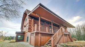A log cabin with a balcony, wooden staircase, and a stone-paved entrance. - < 1 Mi to Kenai River: Spacious Cabin w/ Deck! (Sterling)