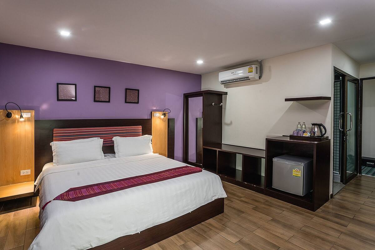 A hotel room with a large bed, a TV, a mini-fridge, and an air conditioning unit.