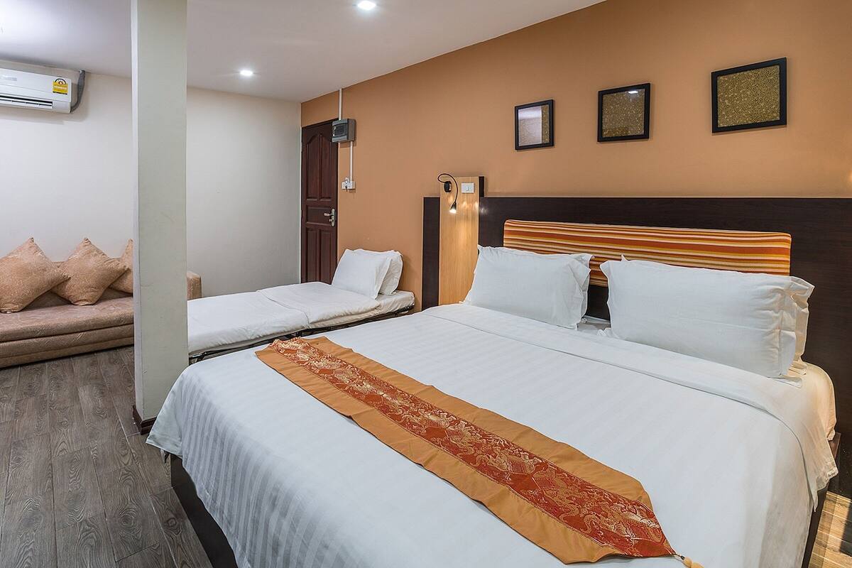 A hotel room with two beds, a sofa, a wooden headboard, and a decorative runner.