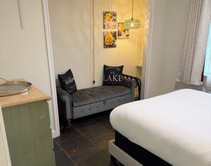 Un dormitorio con cama, un sofá gris, una mesita con bandeja y una pared decorada con cuadros y una lámpara colgante.