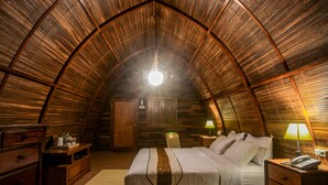 Een gezellig slaapkamer onder de dakpannen met houten lambrisering, een bed, nachtkastjes en een hanglamp.