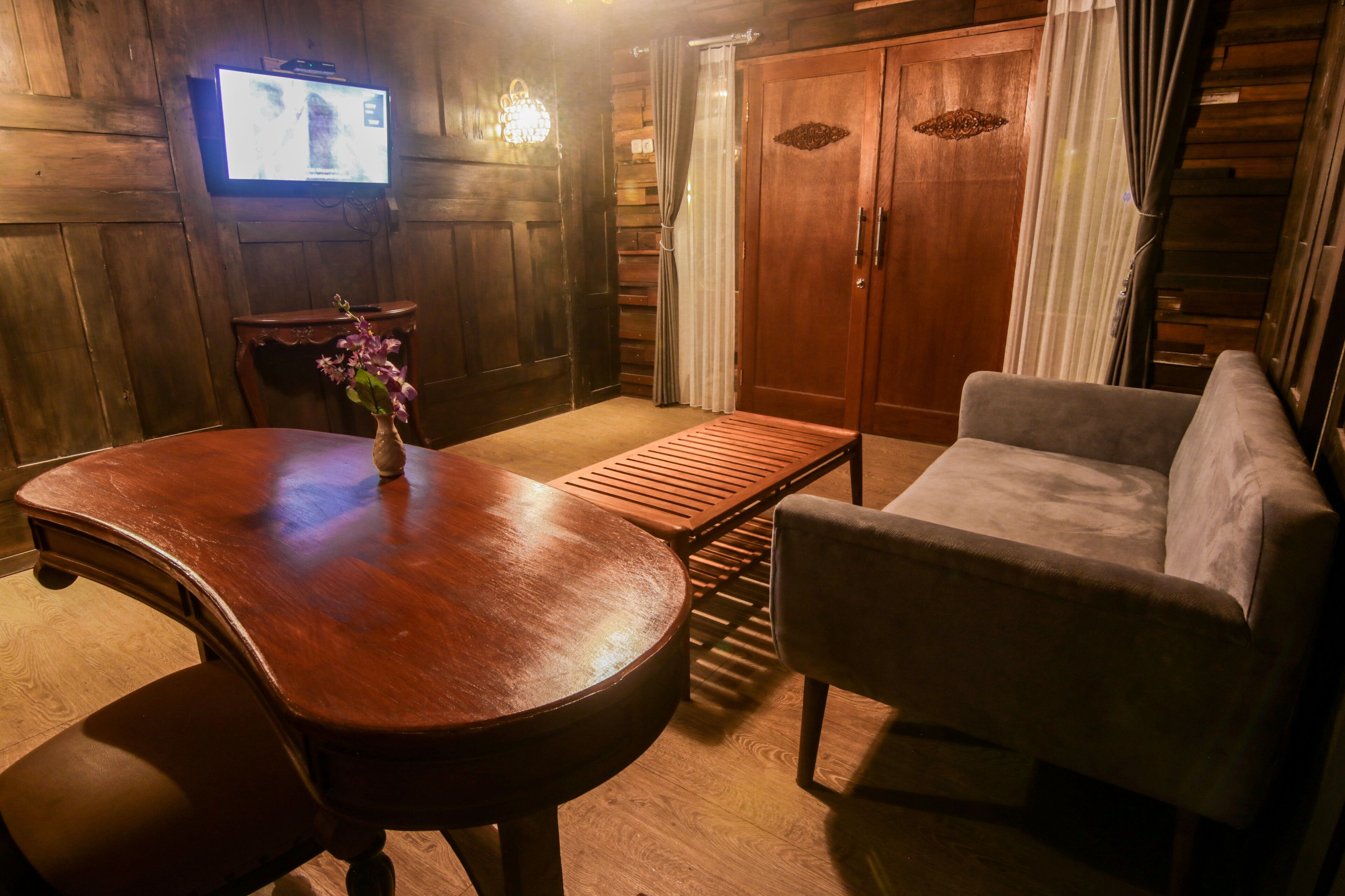A wooden interior with a wooden table, a cushioned chair, a television mounted on the wall, and a wooden wardrobe.