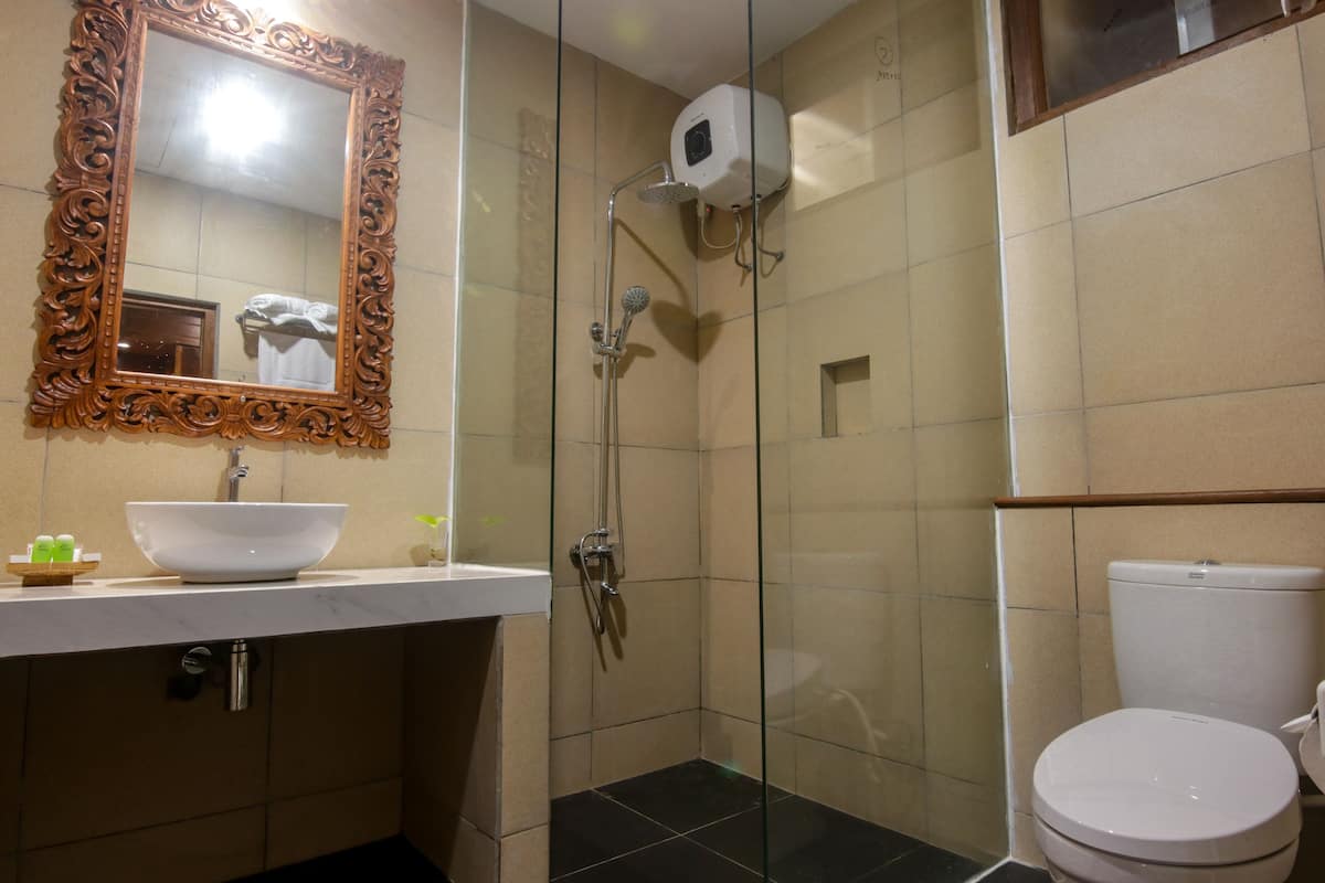 Une salle de bain avec un lavabo blanc, un miroir doté d’un cadre orné, une douche en verre et des toilettes blanches.