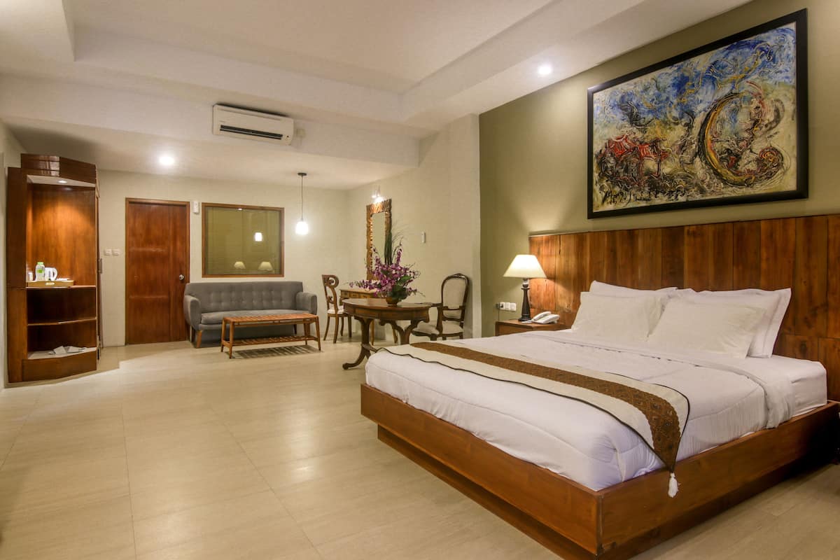 Une chambre d’hôtel avec un grand lit, un canapé, une table avec des chaises et un tableau au mur.