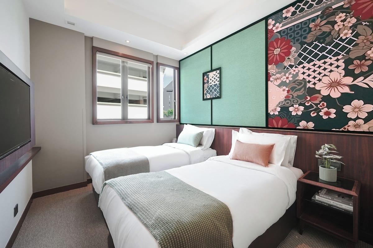 Quarto de hotel com duas camas, televisão, janela e um painel decorativo na parede.