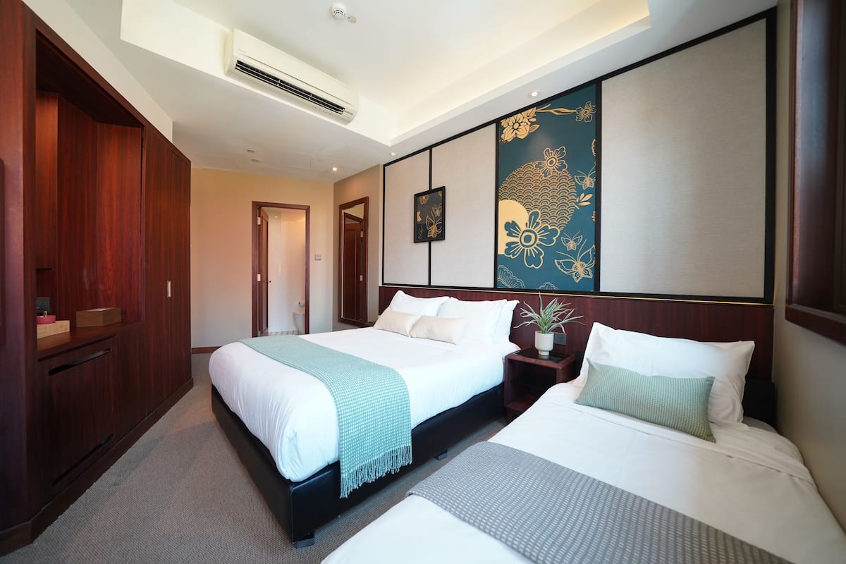 Quarto de hotel com duas camas, um painel decorativo grande na parede, um guarda-roupa de madeira e um aparelho de ar condicionado instalado no teto.