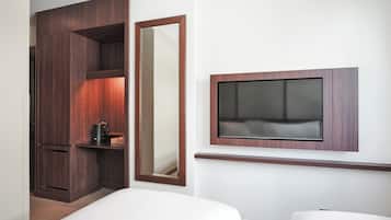 A hotel room with a bed, a TV mounted on the wall, a wardrobe, and a mirror.
