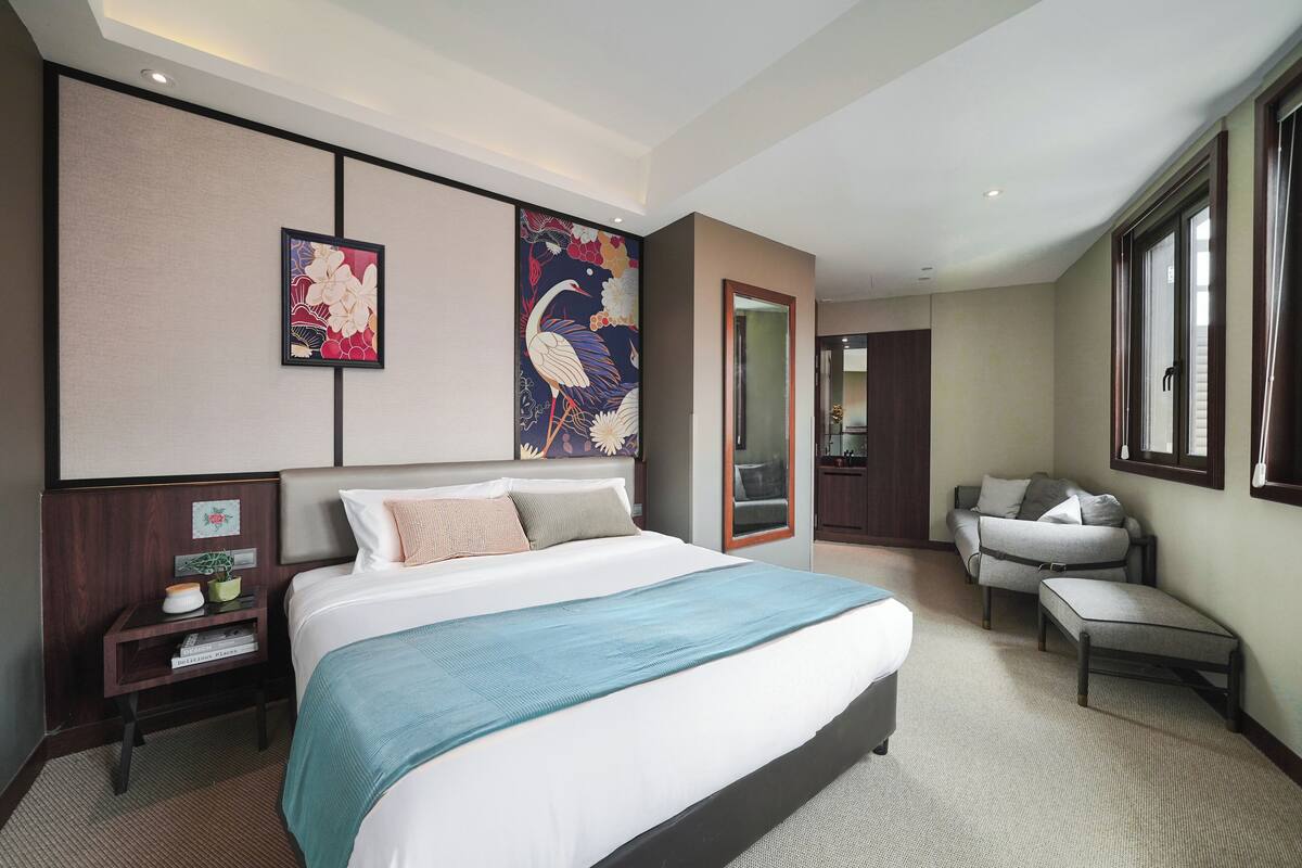 Quarto de hotel moderno com uma cama grande, um espaço de estar com uma poltrona e uma obra de arte de grandes dimensões na parede.