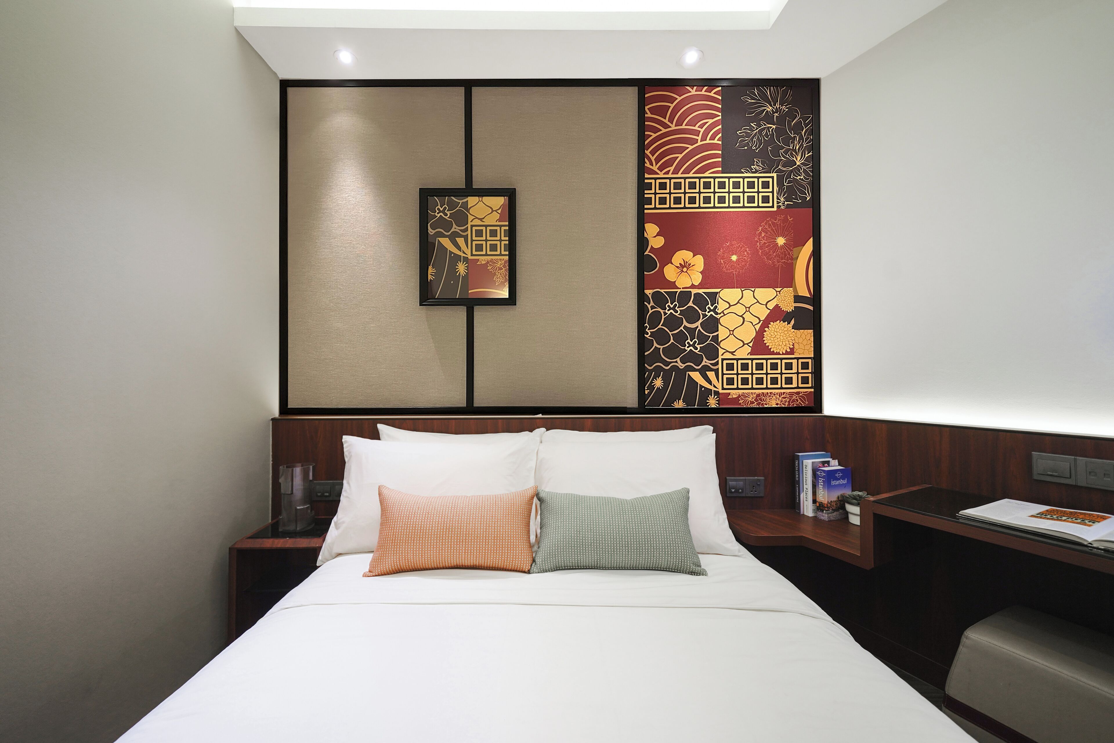 Habitación de hotel con cama, dos almohadas, mesita de noche y pared decorada con paneles.