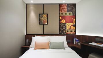 Habitación de hotel con cama, dos almohadas, mesita de noche y pared decorada con paneles.
