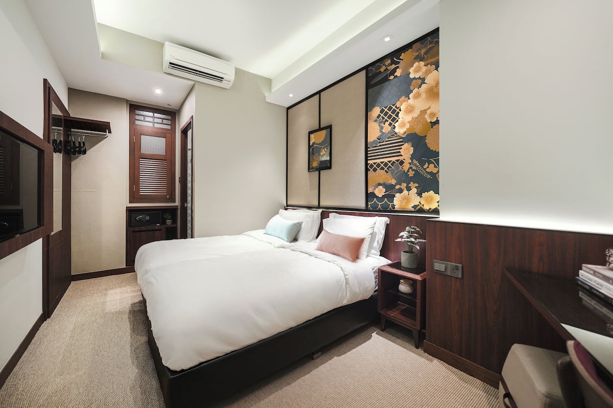Quarto de hotel moderno com uma cama grande, cabeceira de madeira, mesa de cabeceira pequena e ar condicionado fixado na parede.