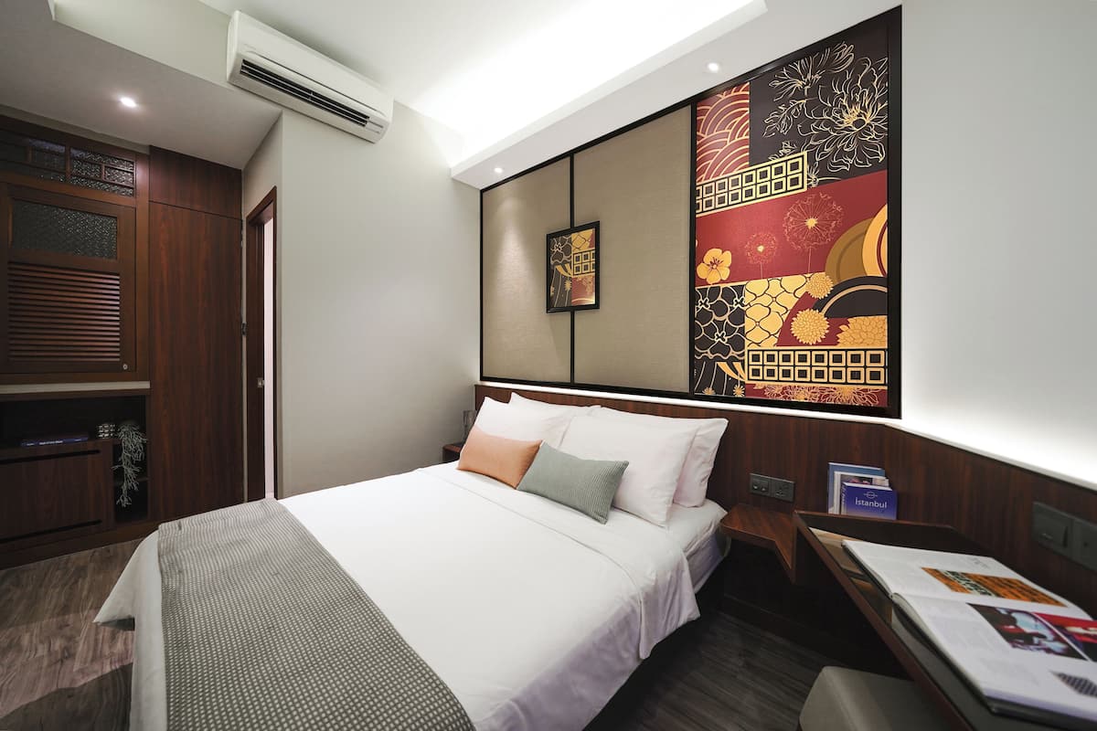Quarto de hotel com cama bem arrumada, escrivaninha com cadeira e um grande painel decorativo na parede.