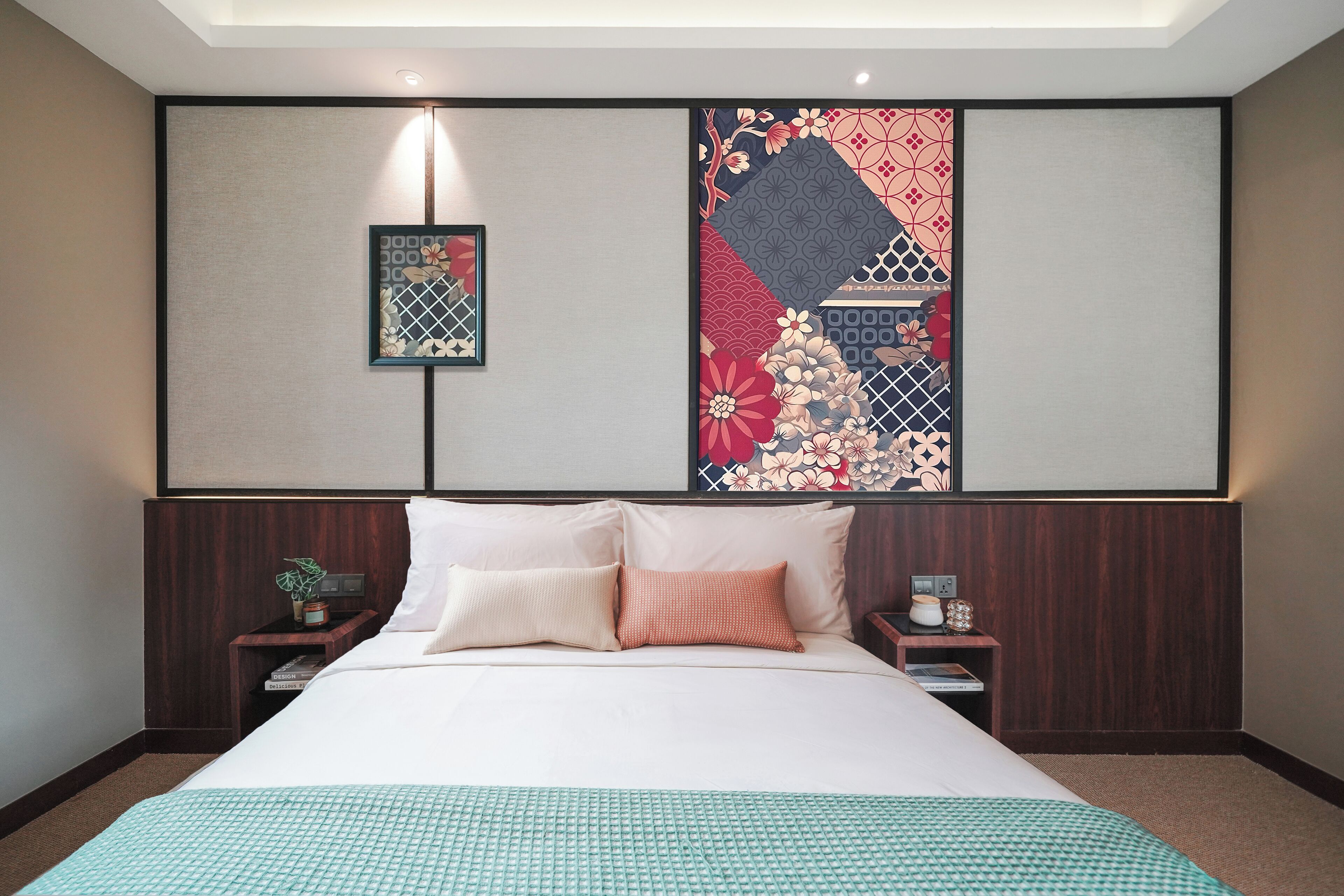 Camera d'albergo con un letto grande, due comodini, un tavolino e una parete con pannelli decorativi, illuminata da una luce a soffitto.
