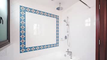 A bathroom with a white tiled wall, a decorative blue and white tile border, a shower, and a white bathtub.