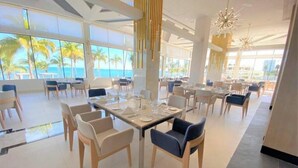 A spacious dining area with tables set for service, large windows offering a view of the ocean, and modern decor with hanging light fixtures. - Enjoy 2026 Christmas Week in a 3-bdm Loft with Rooftop Terrace at Garza Blanca (Cancún)
