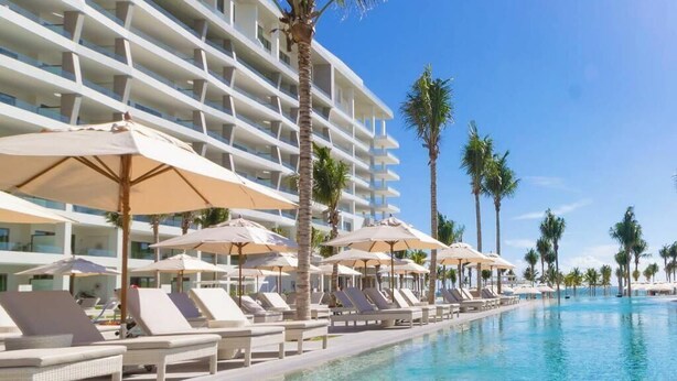 A hotel pool area with sun loungers and umbrellas, surrounded by palm trees and a multi-story building. - Enjoy 2026 Christmas Week in a 3-bdm Loft with Rooftop Terrace at Garza Blanca (Cancún)
