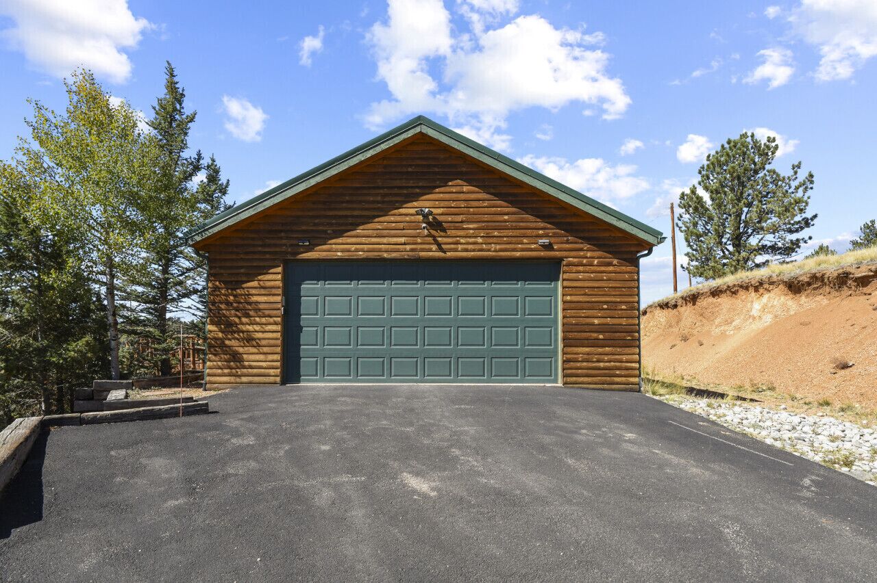 A log cabin with a green garage door, surrounded by trees and a clear sky.