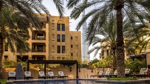 A pool area with lounge chairs, palm trees, and a building with balconies. - Stylish & Spacious Apartment in Downtown Dubai (Dubai)