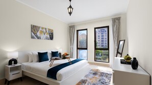 A modern hotel room with a large bed, bedside tables, a nightstand, a desk, a lamp, a painting, a window with curtains, and a view of buildings. - Stylish & Spacious Apartment in Downtown Dubai (Dubai)