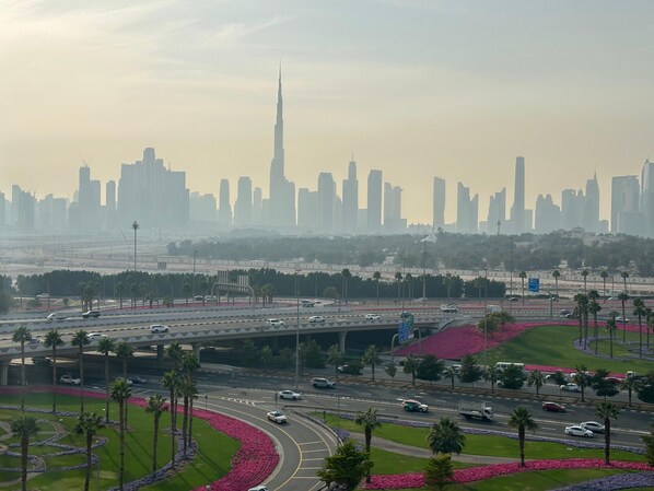 A cityscape with a prominent skyscraper, a highway with vehicles, and landscaped areas with palm trees. - Sunset Haven - Chic Creek Studio (Dubai)
