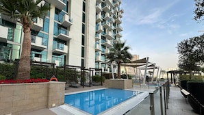 A modern building with a swimming pool, lounge chairs, and palm trees. - Sunset Haven - Chic Creek Studio (Dubai)