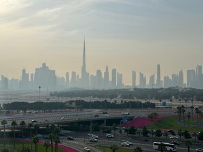 A cityscape with a prominent skyscraper, a highway with vehicles, and a landscaped area with palm trees. - Sunset Haven - Chic Creek Studio (Dubai)