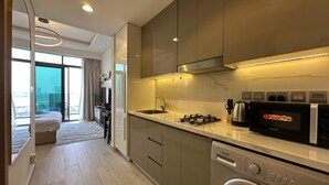 A modern kitchen with a built-in washer and dryer, a microwave, and a gas stove. - Sunset Haven - Chic Creek Studio (Dubai)