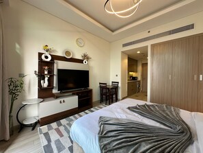 A modern hotel room with a large bed, a flat-screen TV mounted on a wooden console, a dining area with a table and chairs, and a kitchenette. - Sunset Haven - Chic Creek Studio (Dubai)