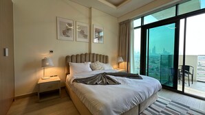A modern hotel room with a large bed, two bedside tables with lamps, a view of the city through large windows, and artwork on the wall. - Sunset Haven - Chic Creek Studio (Dubai)