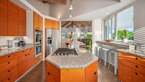 A modern kitchen with wooden cabinets, stainless steel appliances, and a central island with stools. - Hanalei Vista Estate (Princeville)